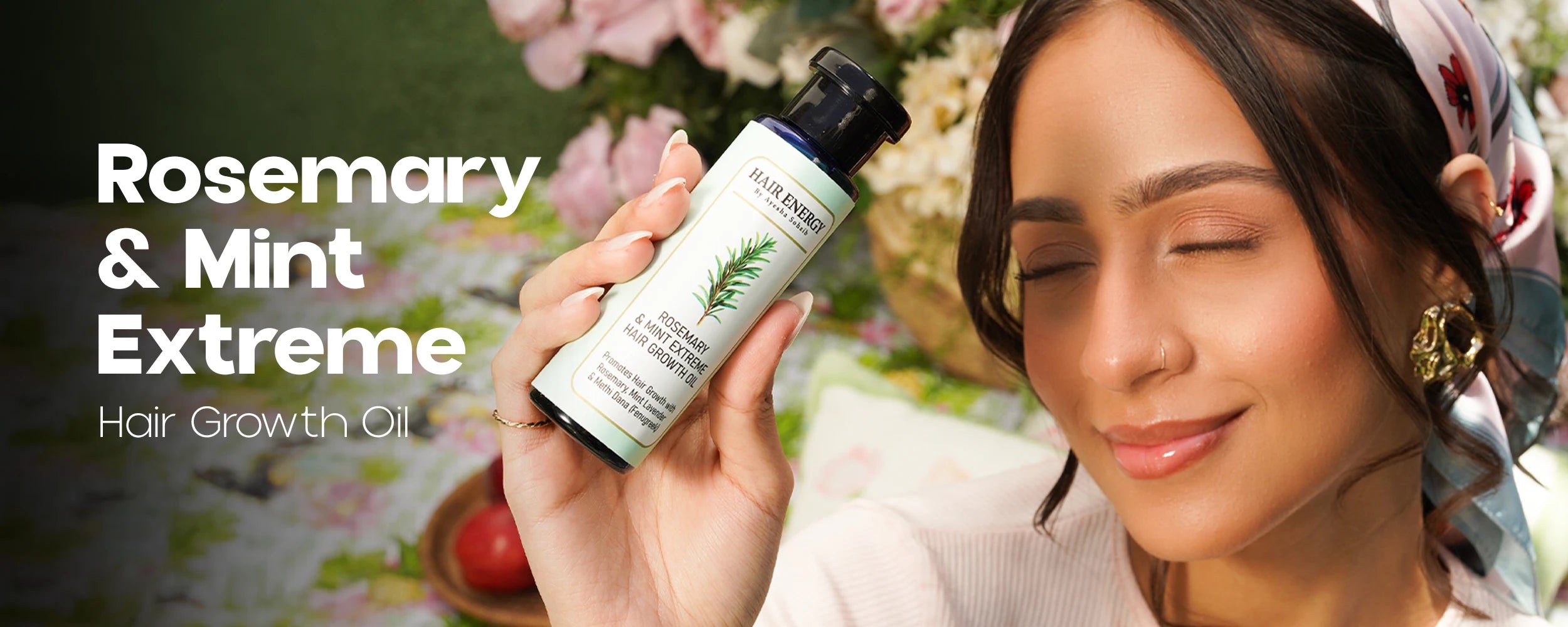 Woman holding a bottle of 'Rosemary & Mint Extreme Hair Growth Oil' with a blurred floral background